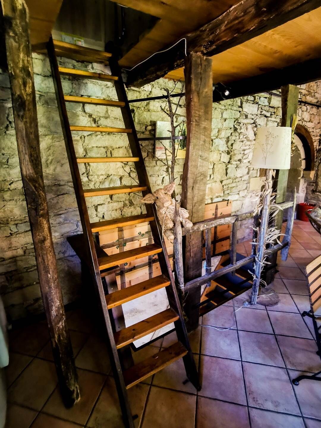 A rustic staircase with a wooden handrail, a stone wall, and a tiled floor.