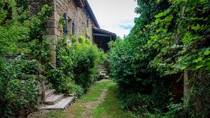 A narrow stone pathway flanked by lush greenery and a stone building with a covered entrance.