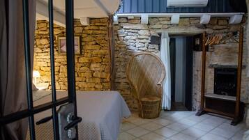 A cozy room with a stone wall, a wicker chair, a fireplace, and a bed with a white bedspread.