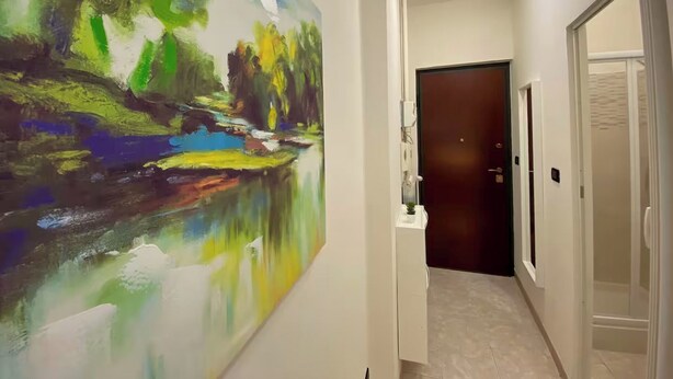 A hallway with a large abstract painting on the left, a door at the end, and a small table with a vase. - Torino Santa Rita (Turin)