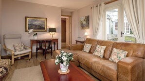 A cozy living room with a leather sofa, a wooden coffee table, a chair, and a vase of flowers. There are two lamps on side tables, and a painting on the wall.