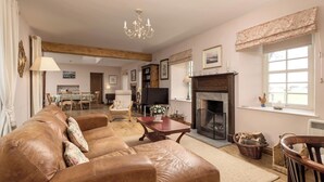 A cozy living room with a leather sofa, a fireplace, and a dining area in the background.