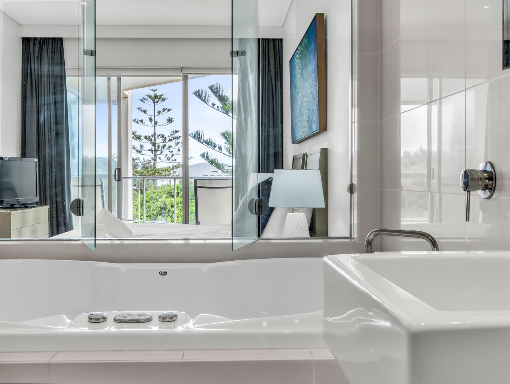 Un bagno moderno con una grande vasca da bagno, box doccia in vetro e vista sul verde.