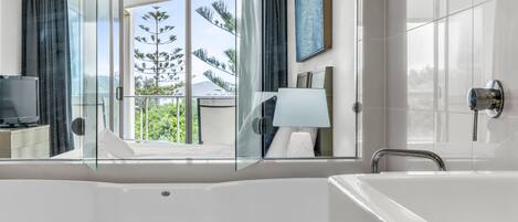 Un bagno moderno con una grande vasca da bagno, box doccia in vetro e vista sul verde.