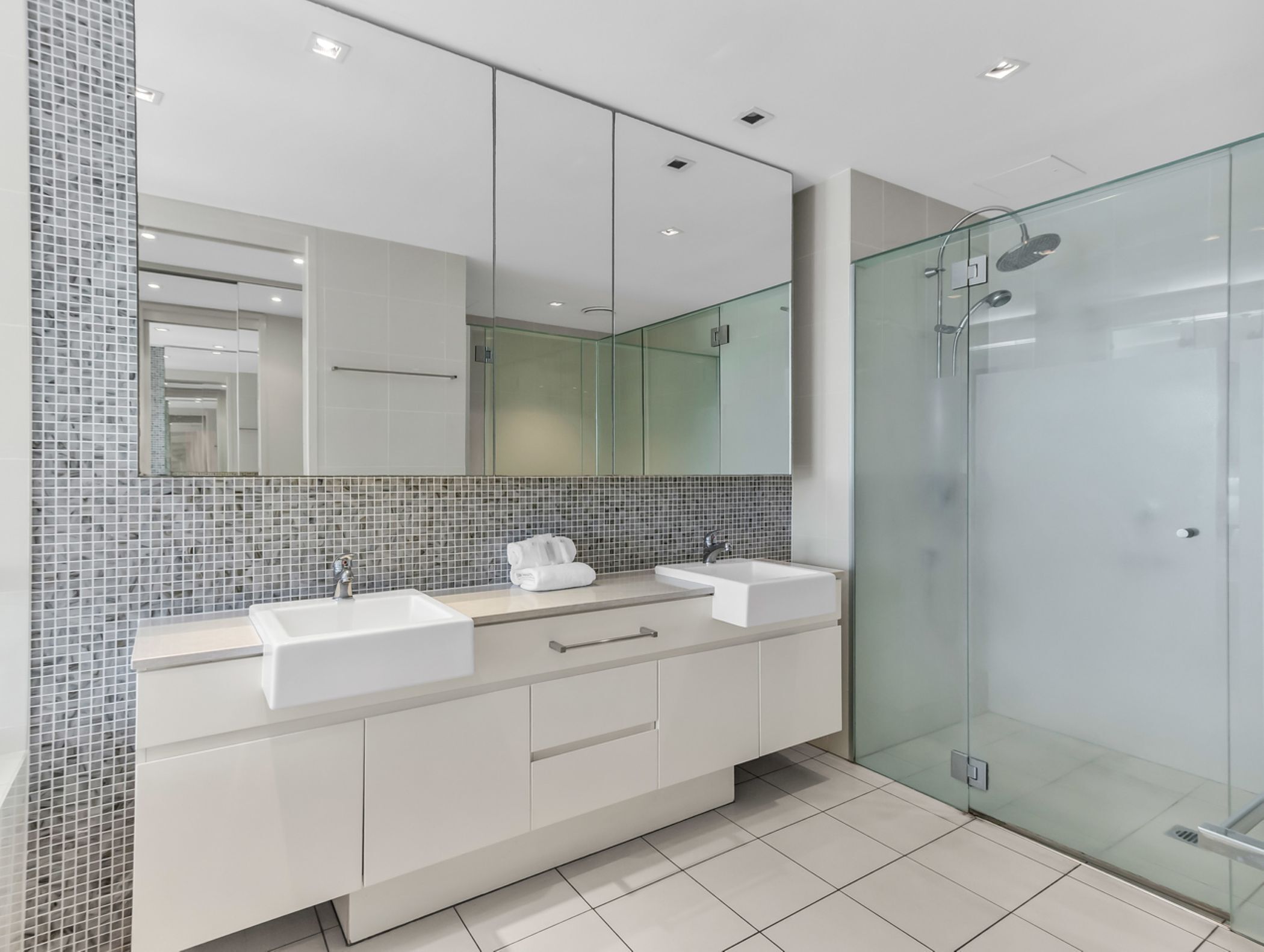 Un baño moderno con dos lavamanos, un espejo grande y una cabina de ducha de vidrio.