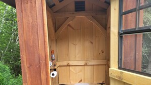 Una cabaña de madera con un inodoro sencillo de madera y una ventana.