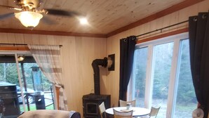 Acogedora habitación tipo cabaña con cama, banca de madera, chimenea y zona de comedor con sillas y mesa.