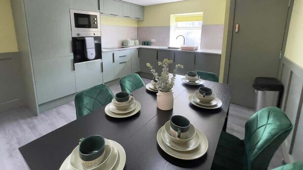Una cucina moderna con mobili grigi, un forno a microonde e una zona pranzo con un tavolo scuro imbandito per quattro persone.