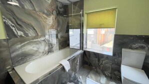 Un bagno moderno con parete in marmo, una vasca e un water.
