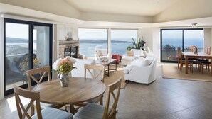 A spacious living room with a large window overlooking the sea, a fireplace, and a dining area with a view.