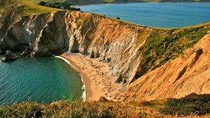 A coastal landscape with cliffs, a beach, and a body of water.