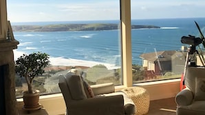 A room with a large window overlooking a coastal view, a potted plant, and a telescope.