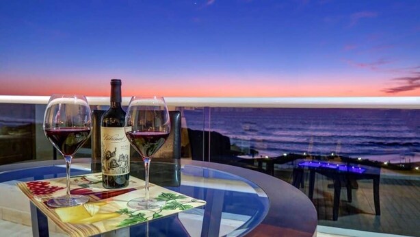 Une table avec deux verres à vin et une bouteille, donnant sur l’océan au coucher du soleil.