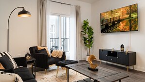 Una sala de estar moderna con un sofá negro, una mesa de centro, una lámpara de pie, una planta en maceta y un televisor montado en la pared.