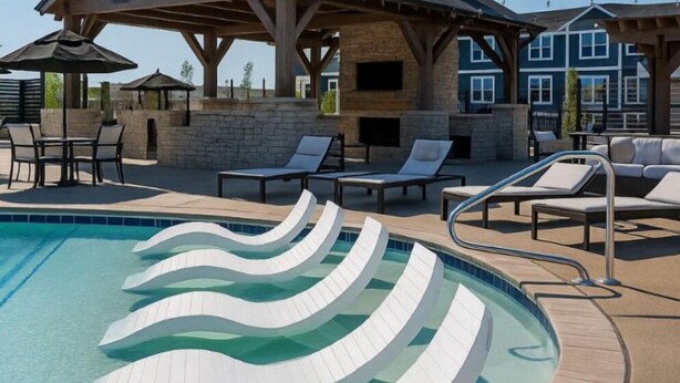 Una piscina con un diseño de borde ondulado único, rodeada de sillones de descanso y un área de estar cubierta con un muro de piedra de fondo.