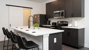 Una cocina moderna con una isla central, armarios oscuros, un refrigerador de acero inoxidable, un microondas, una estufa y un horno empotrado.