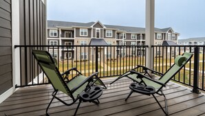 A balcony with two green lounge chairs and a wooden deck.