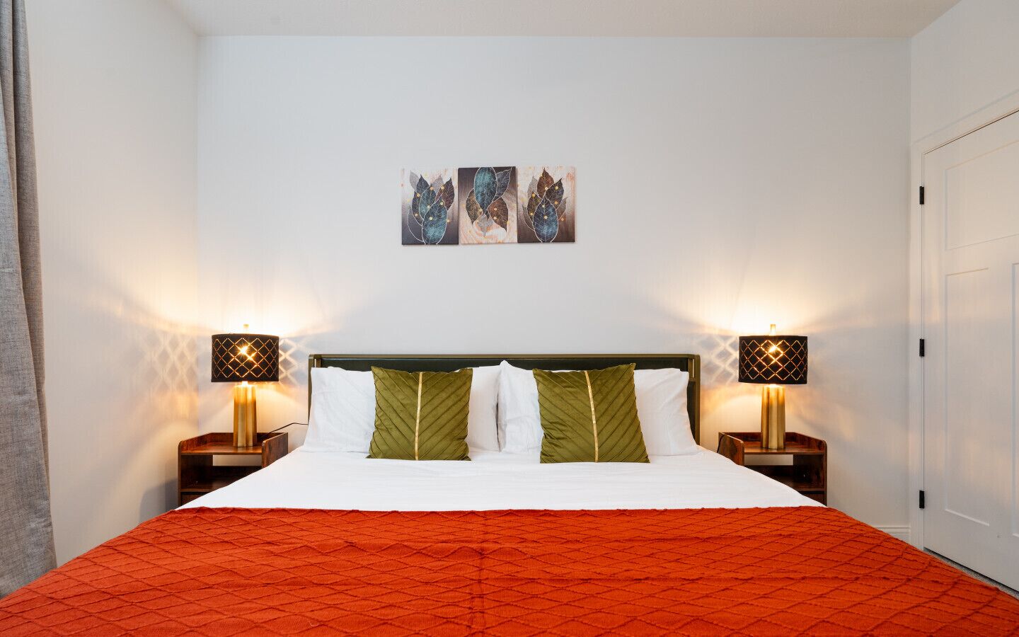 A neatly made bed with a red quilt, two bedside tables with lamps, and three wall-mounted artworks above the bed.