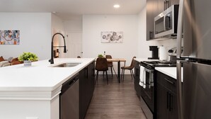 A modern kitchen with a large island, stainless steel appliances, and a dining area with a table and chairs. - Earthy Elegance Spacious 2BR 2BA 2 KingBeds GymWFH (Whitestown)