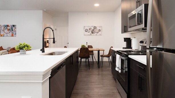 A modern kitchen with a large island, stainless steel appliances, and a dining area with a table and chairs.