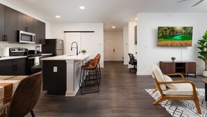 A modern kitchen with dark cabinetry, a central island with bar stools, and a dining area with a wooden table and chairs.