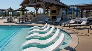 A swimming pool with wavy white steps, lounge chairs, and a covered seating area.