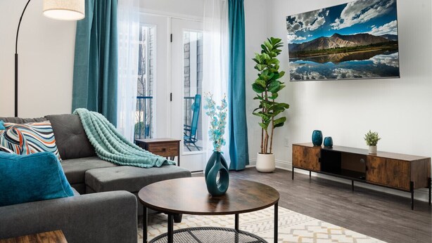 Ein modernes Wohnzimmer mit einem grauen Sofa, einem runden Couchtisch und einem großen Fenster mit blauen Vorhängen.