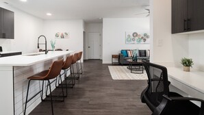 Eine moderne Küche mit weißer Arbeitsplatte, braunen Barhocker und einem Essbereich mit Tisch und Stühlen.