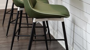 Eine moderne Küche mit weißer Arbeitsplatte, drei grünen Barhocker und einem schwarzen Wasserhahn.