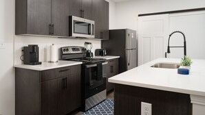 Una cocina moderna con armarios de madera oscura, un refrigerador de acero inoxidable, un microondas, una cafetera y un lavamanos con grifo negro.