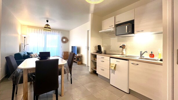 A modern kitchen with a microwave, sink, and dining area with chairs and a table. - Remember - T2 near the ocean (Mimizan)