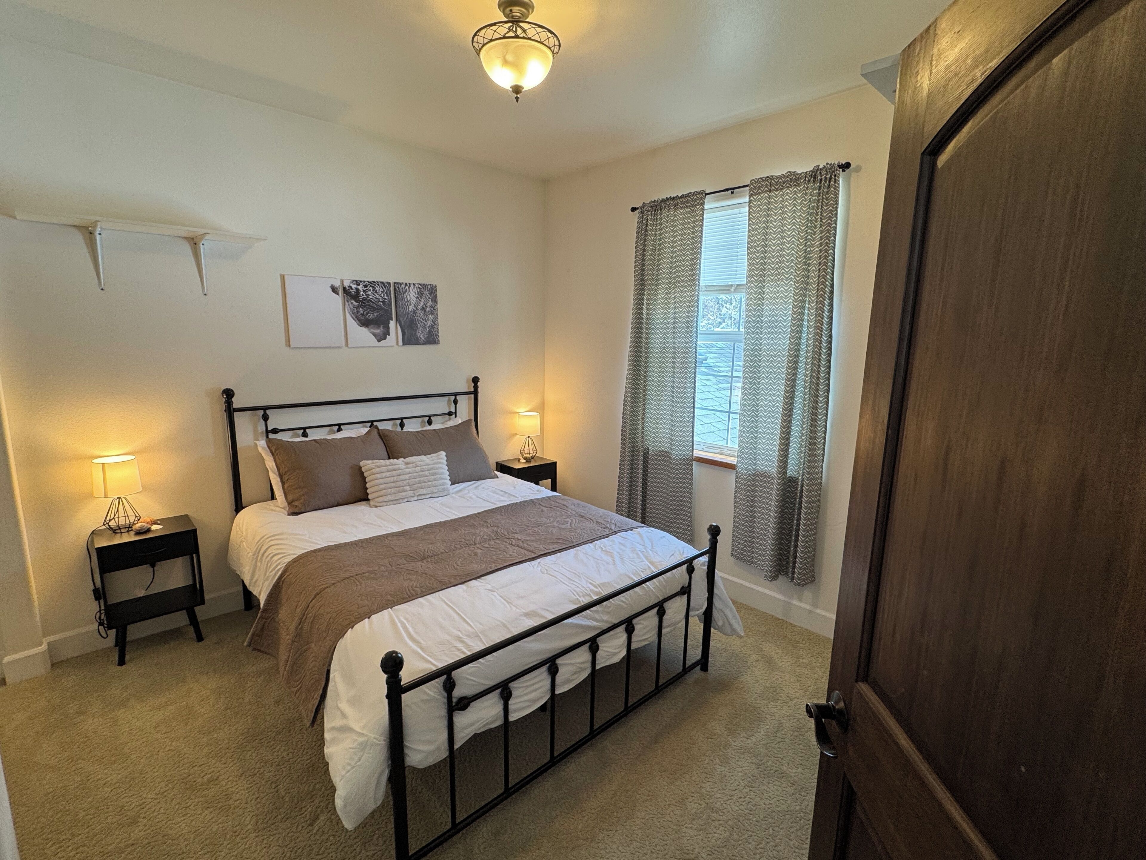 A bedroom with a bed, bedside lamps, a window with curtains, and a door.