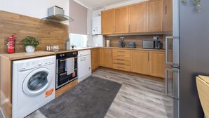 A modern kitchen with wooden cabinets, a built-in oven, a washing machine, and a refrigerator. - Rochester Retreat - Charming 3 Bedroom House (Rochester)