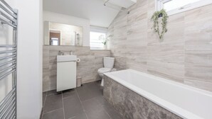 A modern bathroom with a bathtub, toilet, sink, and a mirror. - Rochester Retreat - Charming 3 Bedroom House (Rochester)