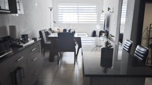 Eine moderne Küche mit Kochinsel, einem Essbereich mit Tisch und Stühlen sowie Blick zum Wohnzimmer durch ein Fenster.
