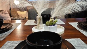 Ein Esstisch mit einer schwarzen Schüssel und Untertasse, einer Vase mit weißen Federn und einem kleinen Topfpflänzchen.