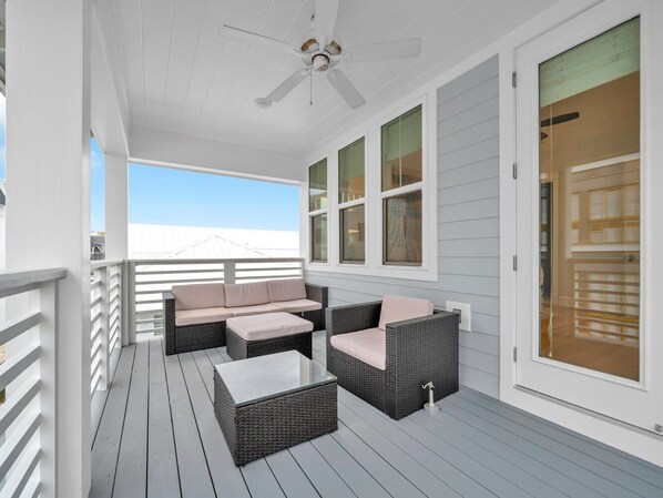 A covered outdoor deck with wicker furniture, a ceiling fan, and large windows. - Golf Cart, Bikes, The Big Chill, Shuttle to Beach Seasonally, 2 Pools! (Alys Beach)