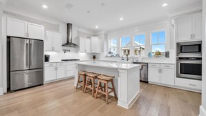 A modern kitchen with white cabinetry, stainless steel appliances, and a central island with stools. - Golf Cart, Bikes, The Big Chill, Shuttle to Beach Seasonally, 2 Pools! (Alys Beach)