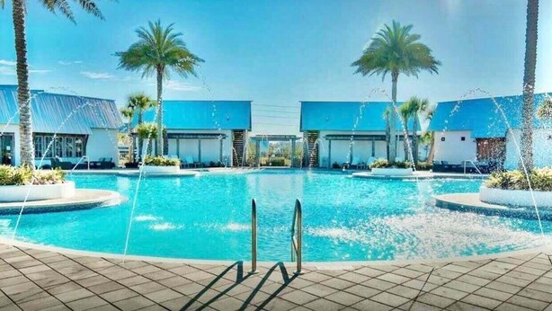 A swimming pool with a clear view of the pool area, surrounded by palm trees and modern buildings with blue roofs. - Golf Cart, Bikes, The Big Chill, Shuttle to Beach Seasonally, 2 Pools! (Alys Beach)
