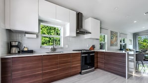 A modern kitchen with a central island, white cabinetry, and a stainless steel range hood.