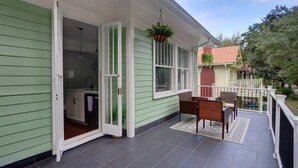 Ett hus med grön fasad, en uteplats, en hängande växt och en matplats med stolar och ett bord.