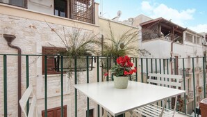 En balkon med et hvidt bord og stole, en potteplante med røde blomster, og udsigt til omkringliggende bygninger.