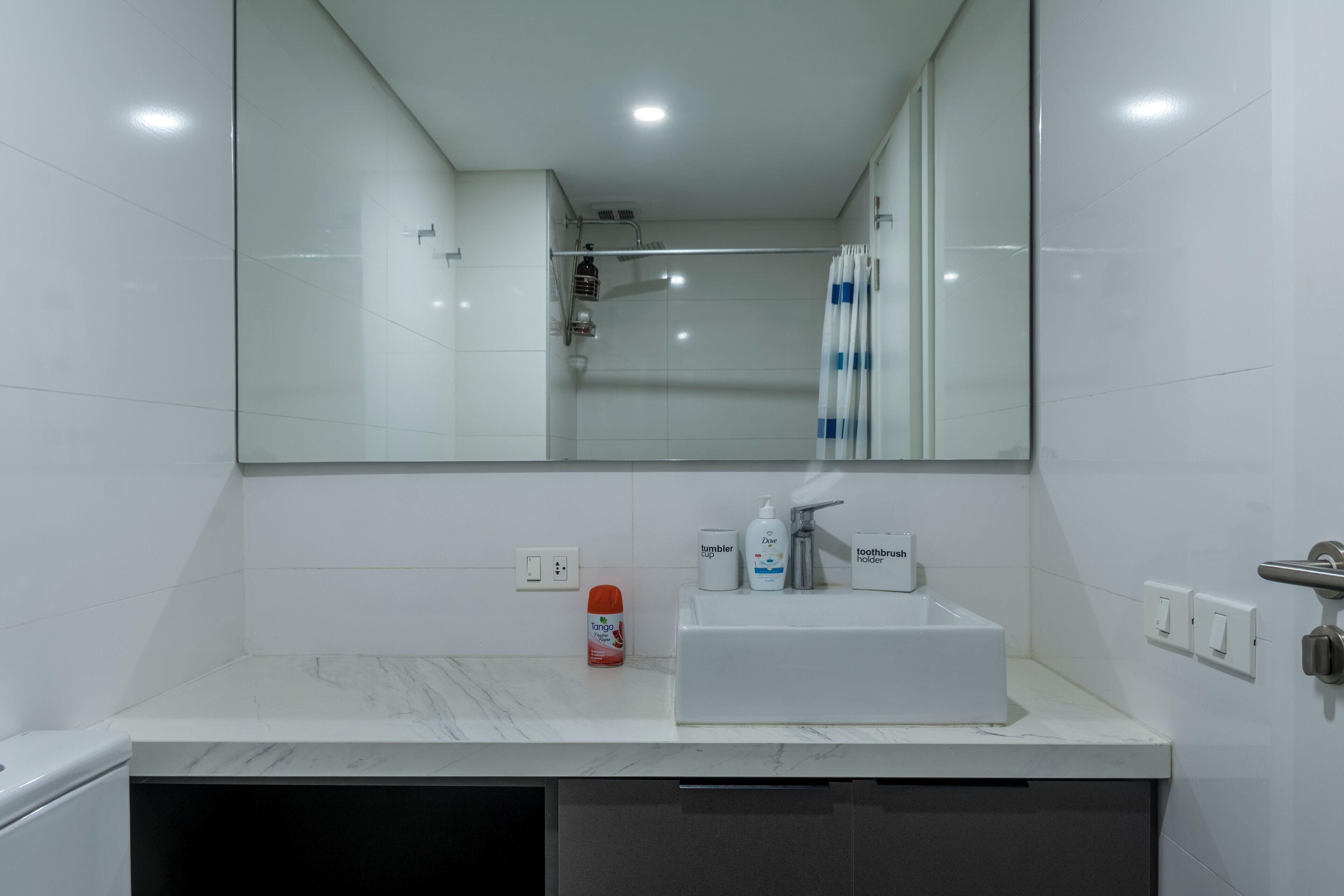 Une salle de bain moderne avec un comptoir en marbre blanc, un grand miroir et une douche dotée d’une porte en verre.
