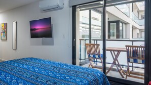 Habitación de hotel con cama, televisión, un cuadro y balcón con sillas y mesa.