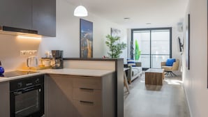 Una cocina moderna con electrodomésticos integrados, una zona de comedor con sofá y mesa de centro, y un amplio ventanal que proporciona luz natural.
