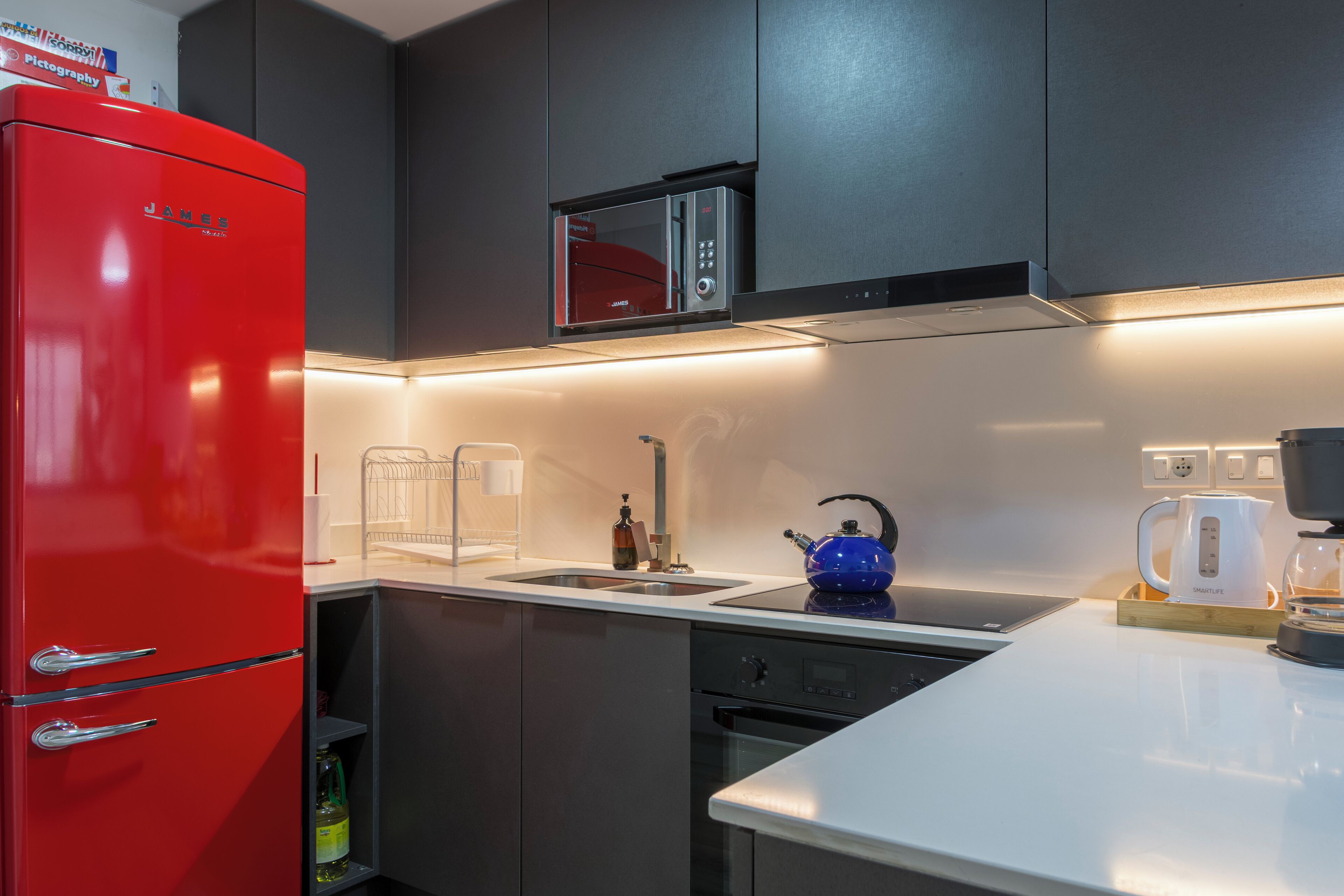 Une cuisine moderne équipée d’un réfrigérateur rouge, d’un four à micro-ondes, d’une bouilloire et d’une machine à café.