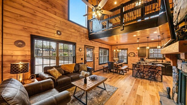 A spacious log cabin interior with a dining area, a fireplace, and a loft with a balcony. - New! Woodridge Lodge! 3 min to PF Pkwy! Pool,Pool Table,Hot Tub,Shuffboard,Poker (Pigeon Forge)