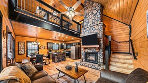 A spacious living area with a fireplace, leather sofas, a dining table, and a kitchen in the background. - New! Woodridge Lodge! 3 min to PF Pkwy! Pool,Pool Table,Hot Tub,Shuffboard,Poker (Pigeon Forge)