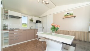 Ett modernt kök med ett fönster, en matplats med bord och stolar samt ett vardagsrum med en soffa och en vägghylla med växter.