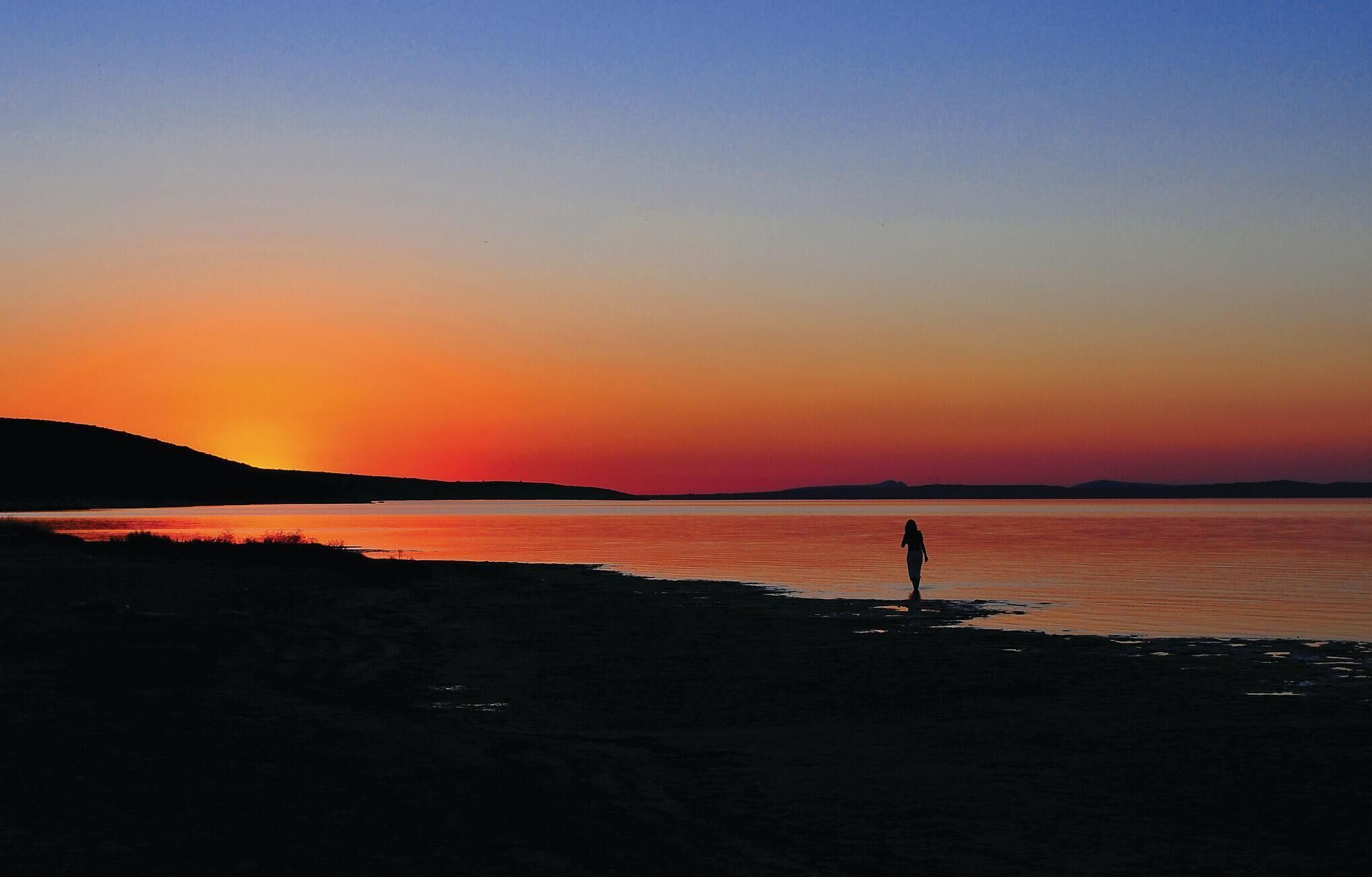 A person standing on a beach during sunset.